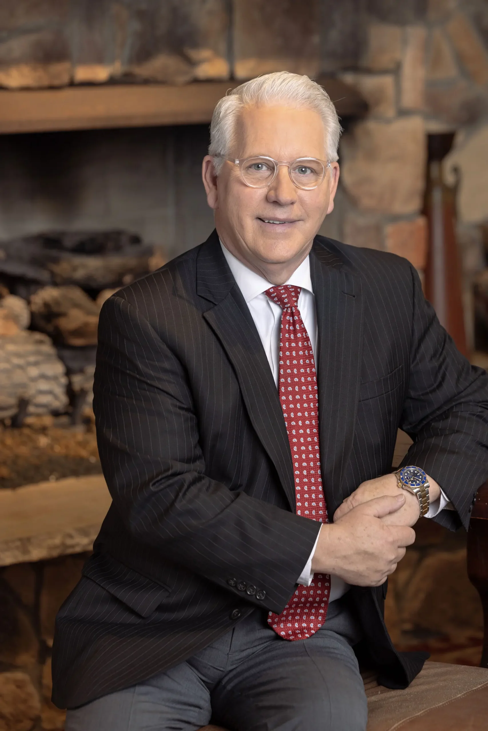 Portrait of Pastor Greg Stephens smiling in front of a wood log fireplace